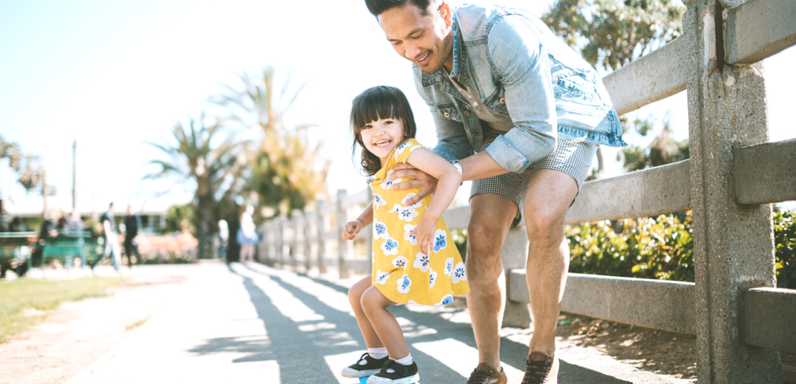 A father took his daughter to the park to practice skateboarding as one of their summertime activities.