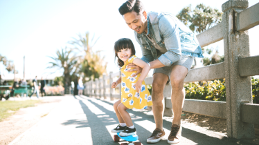 A father took his daughter to the park to practice skateboarding as one of their summertime activities.