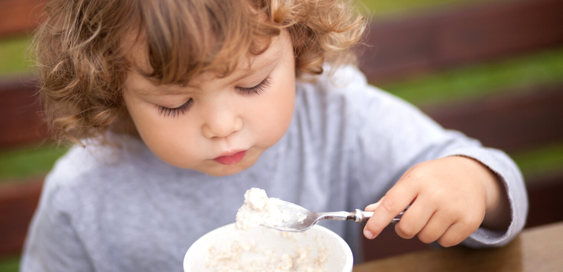 A young girl having her oatmeal outside the house.